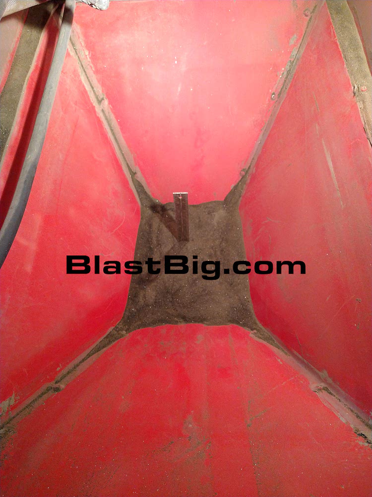 The inside of an abrasive blast cabinet filled with blast media up about 1/3 of the way. A steel 12 inch ruler stands vertically to demonstrate the recommended media depth of approximately 6 to 7 inches.